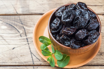 Bowl with tasty dried plums on wooden table Copy space