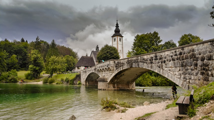 Fototapeta na wymiar Church and bridge on Bohinj lake in Slovenia near the Triglav mountain adn part of Triglav national pak