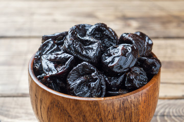 Bowl with tasty dried plums on wooden table