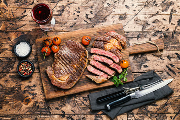 Sliced grilled Medium rare beef steak Ribeye with seasonings and red wine on wooden cutting board, top view