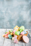 Easter greeting card background with pastel colored eggs and homemade cookies shaped in eggs and bunnies rabbits. With a basket, tulips, rustic wooden table, copy space top view banner