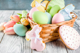 Easter greeting card background with pastel colored eggs and homemade cookies shaped in eggs and bunnies rabbits. With a basket, tulips, rustic wooden table, copy space top view banner