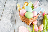 Easter greeting card background with pastel colored eggs and homemade cookies shaped in eggs and bunnies rabbits. With a basket, tulips, rustic wooden table, copy space top view banner