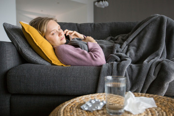 Obraz premium Sick woman lying on sofa and calling doctor on mobile phone