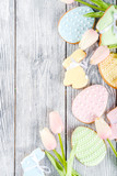Easter greeting card background with pastel colored eggs and homemade cookies shaped in eggs and bunnies rabbits. With a basket, tulips, rustic wooden table, copy space top view banner