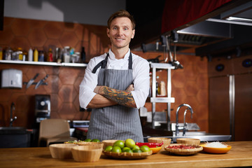 Waist up portrit of handsome chef posing standing at table with spices, copy space