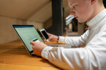 businessman with phone, laptop and card doing electronic payment on his working place f