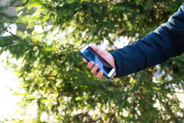 Man's hand is holding smartphone in hand on tree background outdoors. Concept of communication, call, messaging business