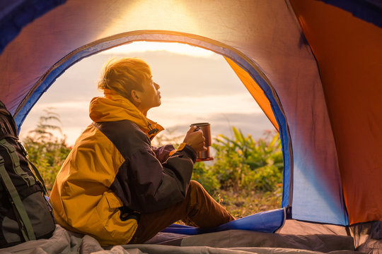 A young man sitting in the tent with drink, looking at the mountain landscape in winter.Light effects - Powered by Adobe