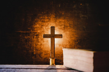 Cross with bible and candle on a old oak wooden table. Beautiful gold background. Religion concept.