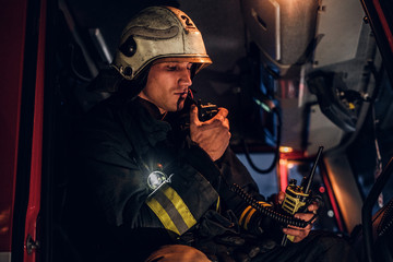 Fototapeta na wymiar The fire brigade arrived at the night-time. Fireman in a protective uniform sitting in the fire truck and talking on the radio