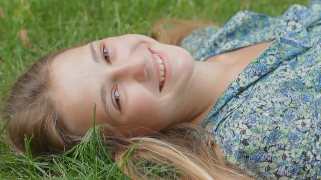 Portrait of teen girl lying on green grass smiling at camera. Happy young woman enjoying nature while resting at the park