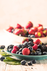 Ripe sweet different berries in a blue bowl on white wooden table. Harvest Concept