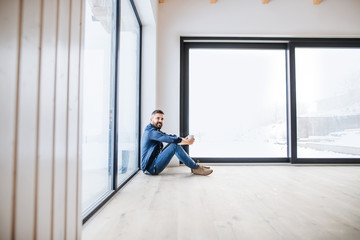 A mature man sitting on the floor in unfurnished new house, holding coffee.