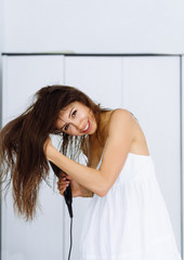 Woman in bathrobe drying her hair with dryer over white background