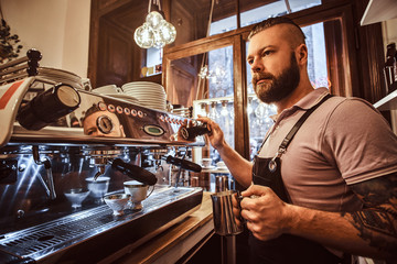 Handsome tattooed barista with stylish beard and hairstyle working on a coffee machine in a coffee shop or restaurant