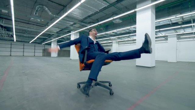 Gappy, funny office manager is riding on a rolling chair across an empty hall