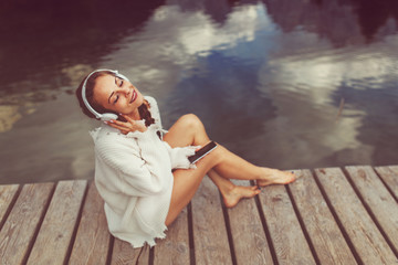 Attractive young woman listening to music via wifi headphones and smartphone on the lake