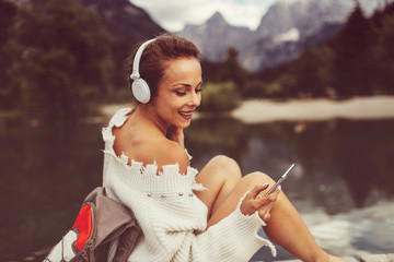 Attractive young woman listening to music via wifi headphones and smartphone on the lake
