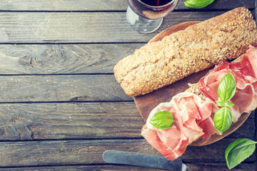 Close up ciabatta sandwich with jamon serrano and basil, on wooden background, top view