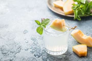 Melon lemonade with ice and mint in a glass on the gray table. Summer refreshing drink.