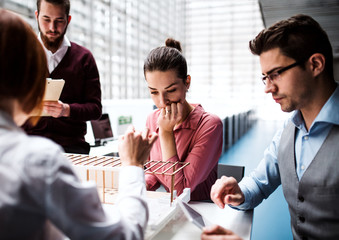 Group of young architects with model of a house standing in office, talking.