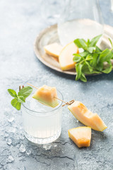 Melon lemonade with ice and mint in a glass on the gray table. Summer refreshing drink.