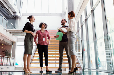 Group of young businesspeople standing near a staircase, talking.