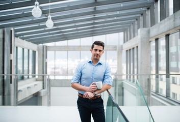 A young businessman with cup of coffee in corridor outside office.