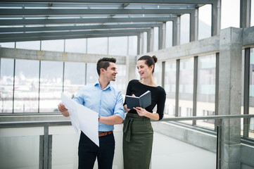 Two young architects with blueprints standing in office, talking.