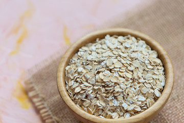 Uncooked oatmeal or oat flakes in a wooden bowl on a pink background