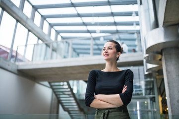 A portrait of young businesswoman standing in corridor outside office, arms crossed.