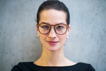 Portrait of young businesswoman with glasses standing in office, looking at camera.