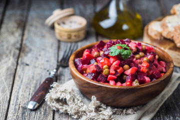 Russian beetroot salad vinaigrette in wooden bowl with rye bread, rustic background
