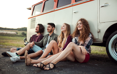 A group of young friends on a roadtrip through countryside, sitting by a minivan.