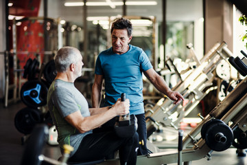 A senior man with a young trainer doing strength workout exercise in gym.