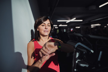 A senior woman in gym resting after doing exercise, checking time.