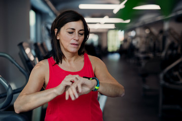 A senior woman in gym resting after doing exercise, checking time.