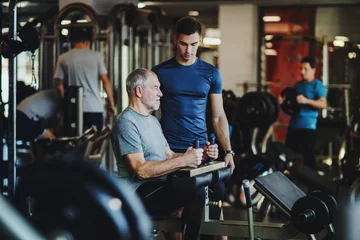 Foto op Aluminium A senior man with a young trainer doing strength workout exercise in gym. © Halfpoint