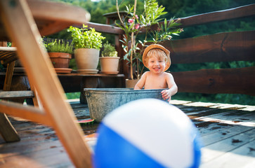 Small boy with a ball in bath outdoors in garden in summer, playing in water.