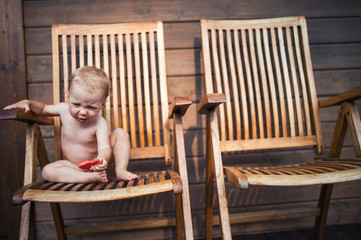 Small girl sitting on wooden chair on a patio in summer, eating watermelon.