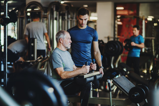 A senior man with a young trainer doing strength workout exercise in gym.