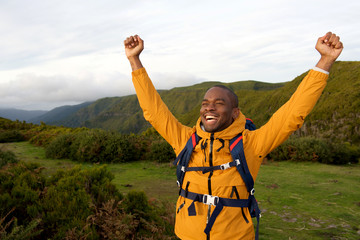 happy african american backpacker standing outdoors with arms raised