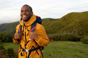 smiling african american hiker walking with backpack in nature
