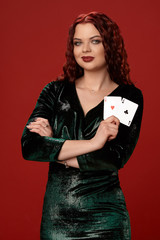 Young sexy woman with a red curly hair holding aces, on a red background. Poker