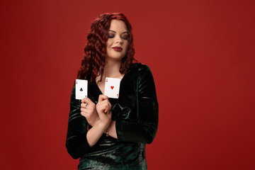 Naklejka premium Young sexy woman with a red curly hair holding aces, on a red background. Poker