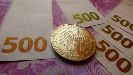 A western ten German Mark coin displayed on 500 Euro banknotes
