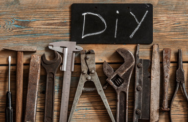Flat lay with different carpentry tools set of hand tools and letters of DIY on a wooden background. Old rusty tools.