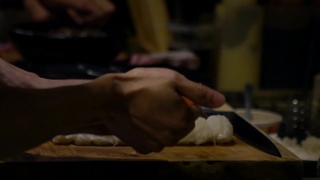 Asian cheff prepare the slice of raw fish for make a sushi in a kitchen of Japan. Man cooking in a japanese restaurant. Close up of hands making delicious asiatic food for sale-Dan