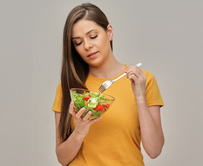 woman dressed in yellow eating salad from glass bowl using fork